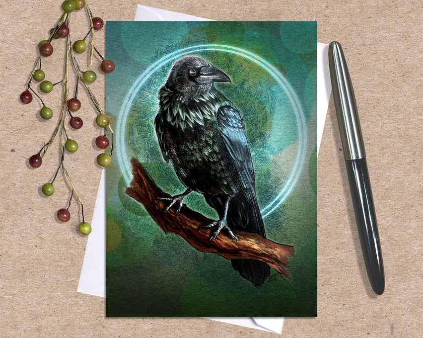 Greeting card with a raven illustration on a wooden surface with a pen and decorative branches.
