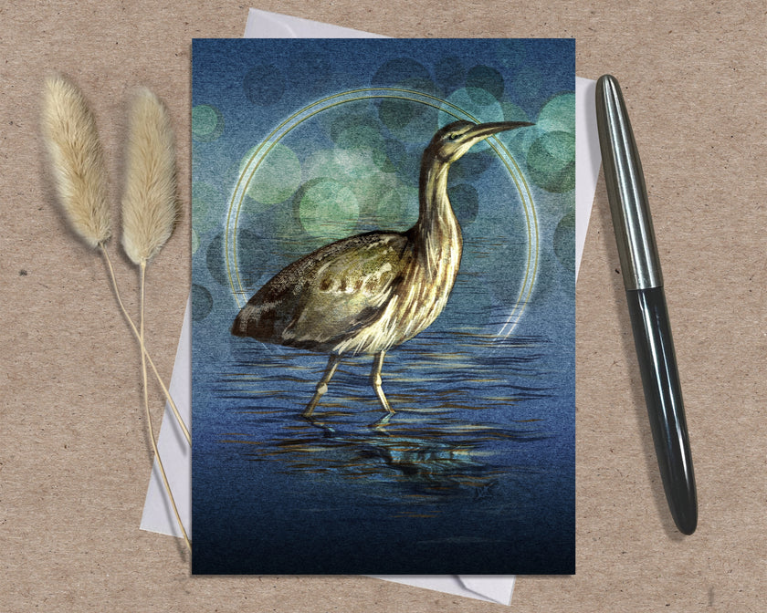 Greeting card with a bittern design on a textured surface with a pen and dried plants.