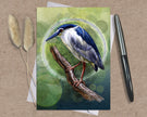 Greeting card with a bird illustration on a wooden surface with a pen and dried plants.