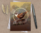 Greeting card with a bird illustration on a textured surface with a pen and dried plants.