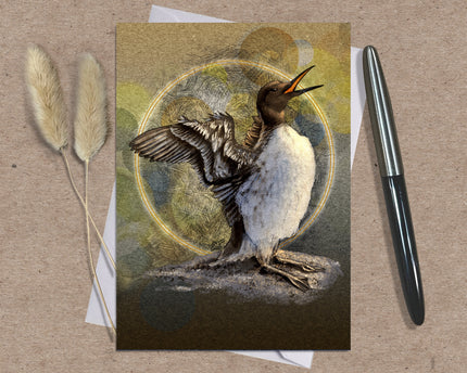 Greeting card with a penguin illustration on a textured surface with a pen and dried plants.