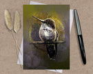 Greeting card with a hummingbird illustration on a textured surface with a pen and dried plants.