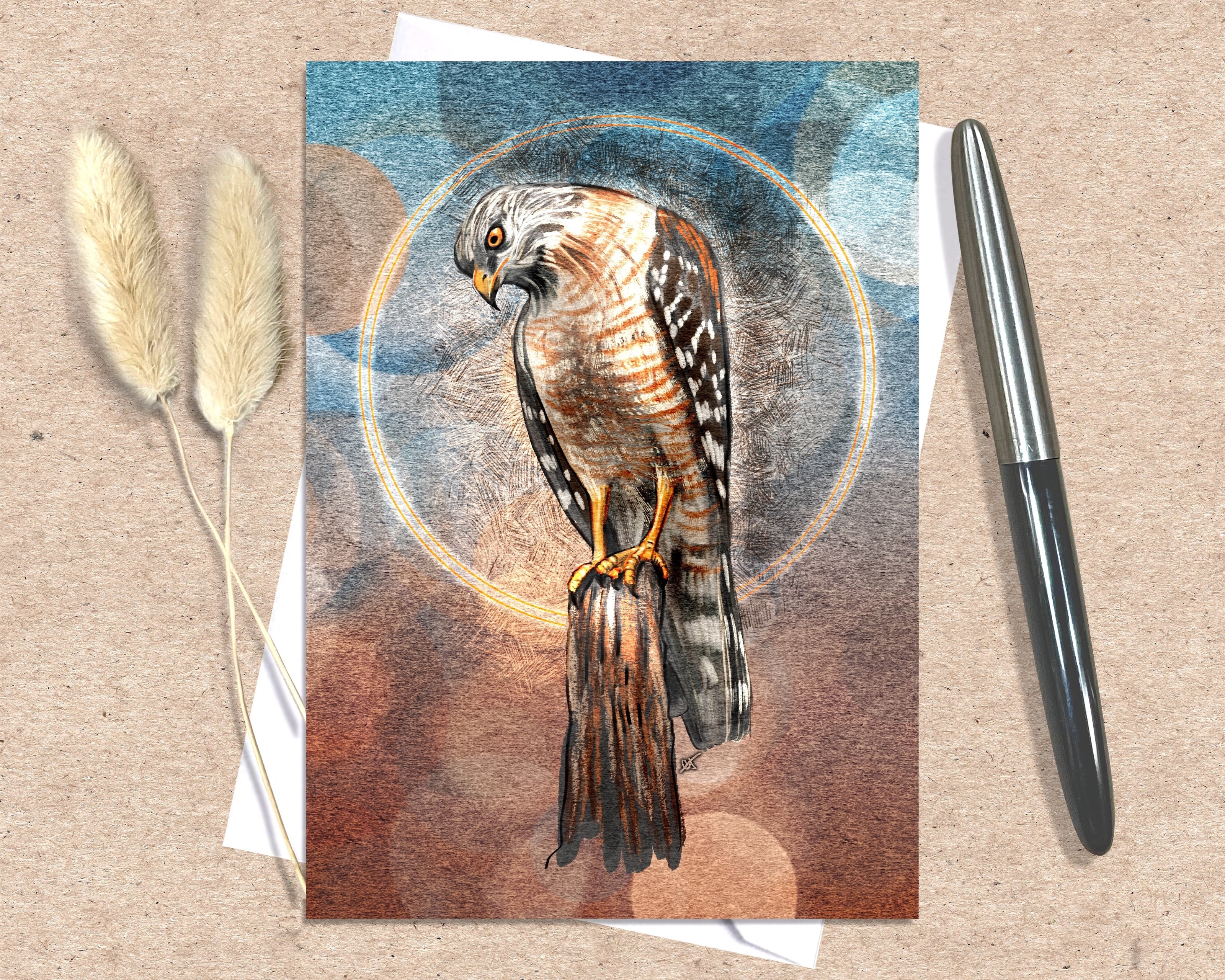 Greeting card with a hawk illustration on a textured surface with a pen and dried plants.