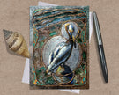 Decorative greeting card with a bird illustration on a textured surface with a shell and pen.