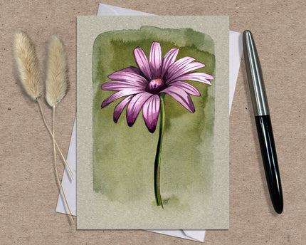 Greeting card with a pink flower illustration on a textured surface with a pen and dried plants.