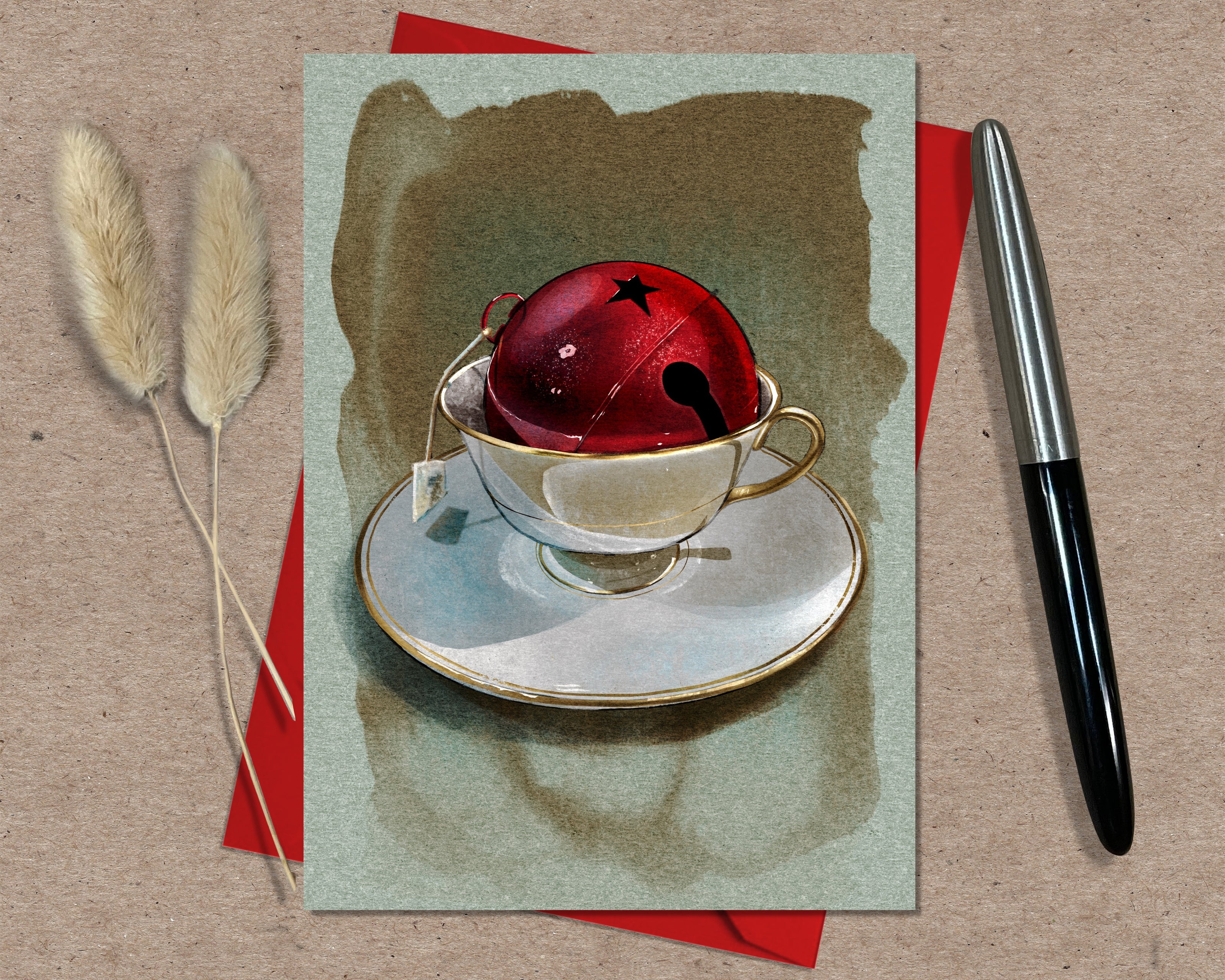 Card with a teacup and red bell on a textured surface with a pen and dried plants.