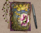 Decorative card with a fairy design on a textured surface with a pen and decorative elements.