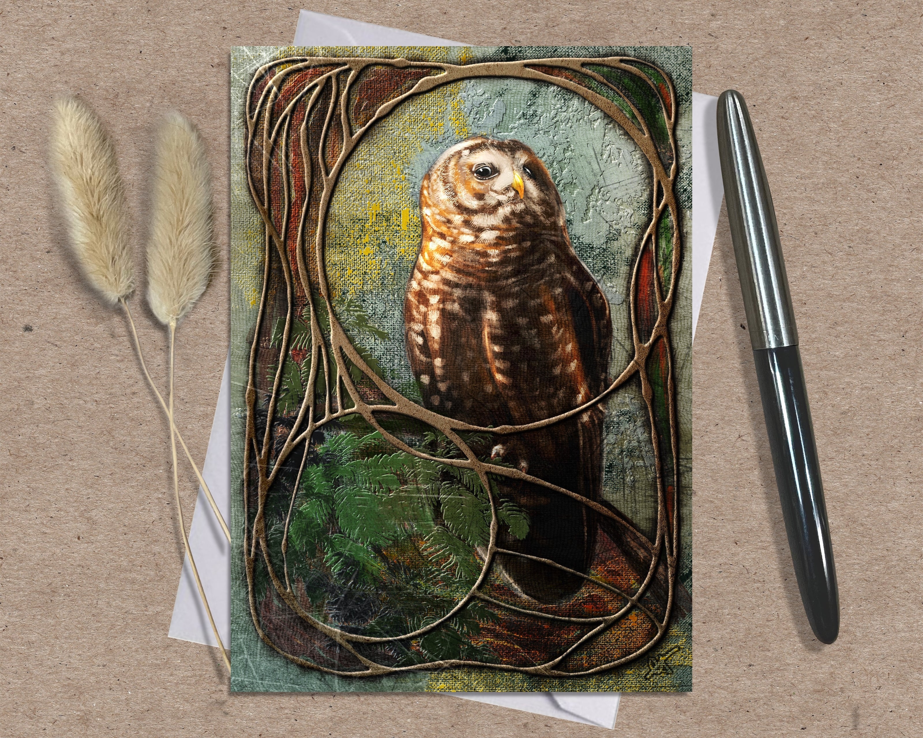 Greeting card with an owl design on a textured surface with a pen and dried plants.