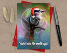Greeting card with a bird wearing a Santa hat and 'Yuletide Greetings!' text, placed on a textured surface with a pen and dried plants.