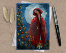 Greeting card with a red-robed figure surrounded by flowers on a textured surface with a pen and dried plants.