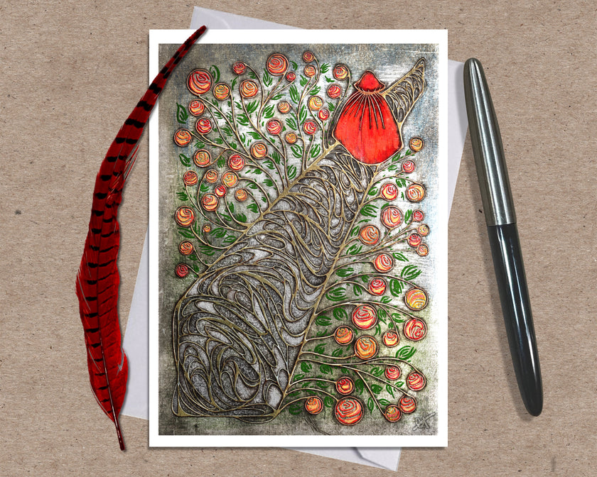 Greeting card with a stylized tree design featuring flowers and a person in a red cloak placed on a textured surface with a pen and feather.