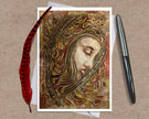 Greeting card with artistic design of a face surrounded by feathers and leaves, accompanied by a pen and feather on a textured surface.