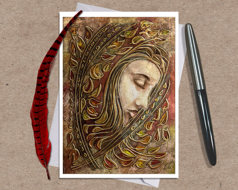 Greeting card with artistic design of a face surrounded by feathers and leaves, accompanied by a pen and feather on a textured surface.
