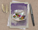 Greeting card with a teacup design on a textured surface with a pen and dried plants.