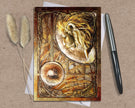 Decorative greeting card with lion design on a textured surface with a pen and dried plants.