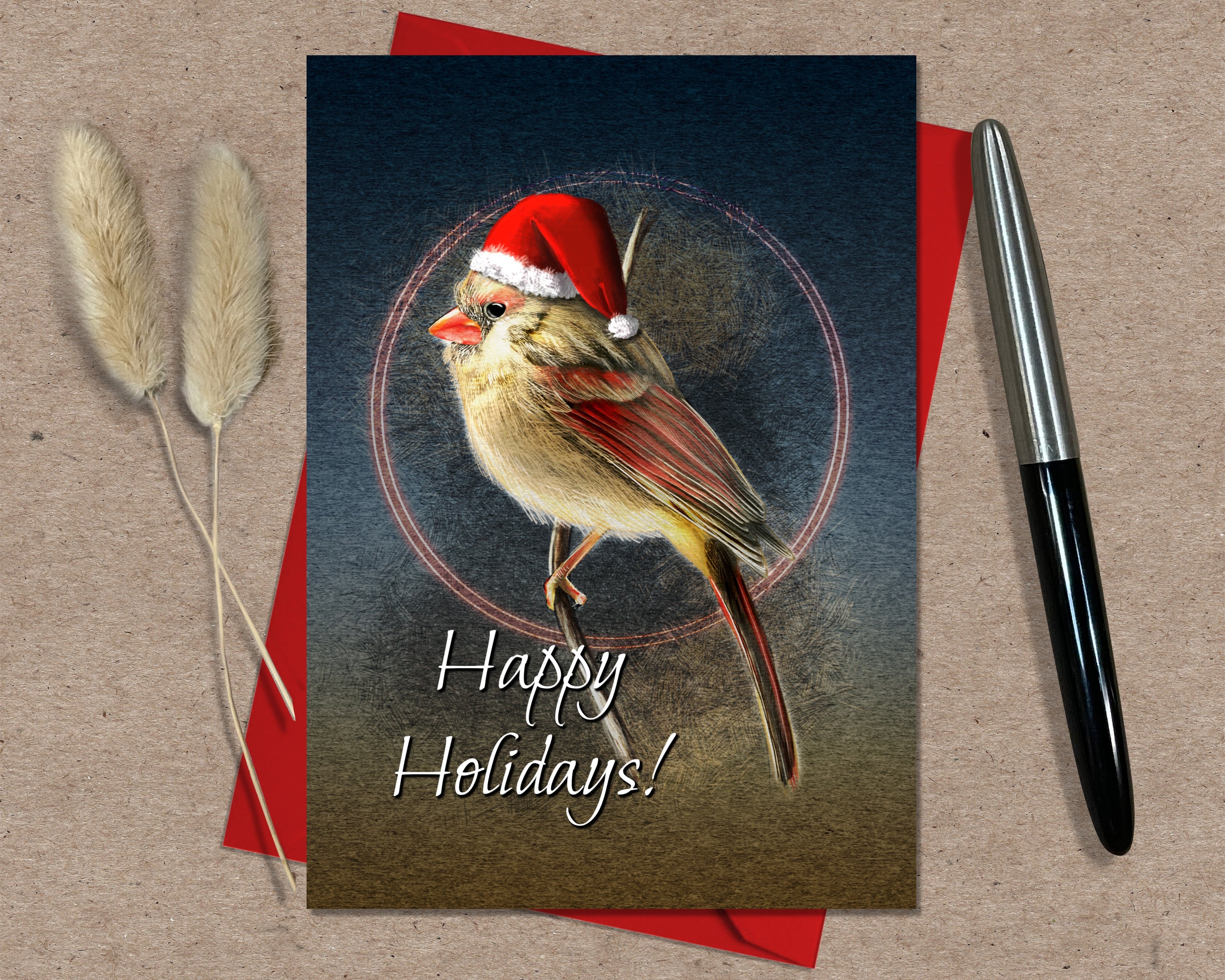 Christmas card with a bird wearing a Santa hat and 'Happy Holidays!' text, placed on a textured surface with a pen and dried plants.