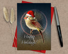 Christmas card with a bird wearing a Santa hat and 'Happy Holidays!' text, placed on a textured surface with a pen and dried plants.