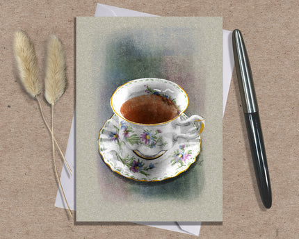 Greeting card with a teacup illustration on a textured surface with a pen and dried plants.