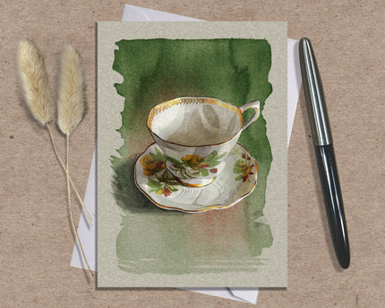 Greeting card with a teacup design on a textured surface with a pen and dried plants.