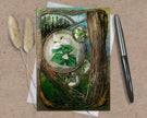 Decorative card with floral design on a textured surface with a pen and dried plants.