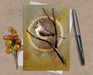 Greeting card with a bird illustration on a branch, surrounded by berries and a pen on a textured surface.