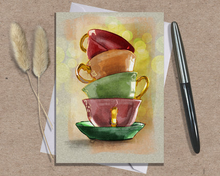 Greeting card with a stack of colorful teacups on a textured surface with a pen and dried plants.