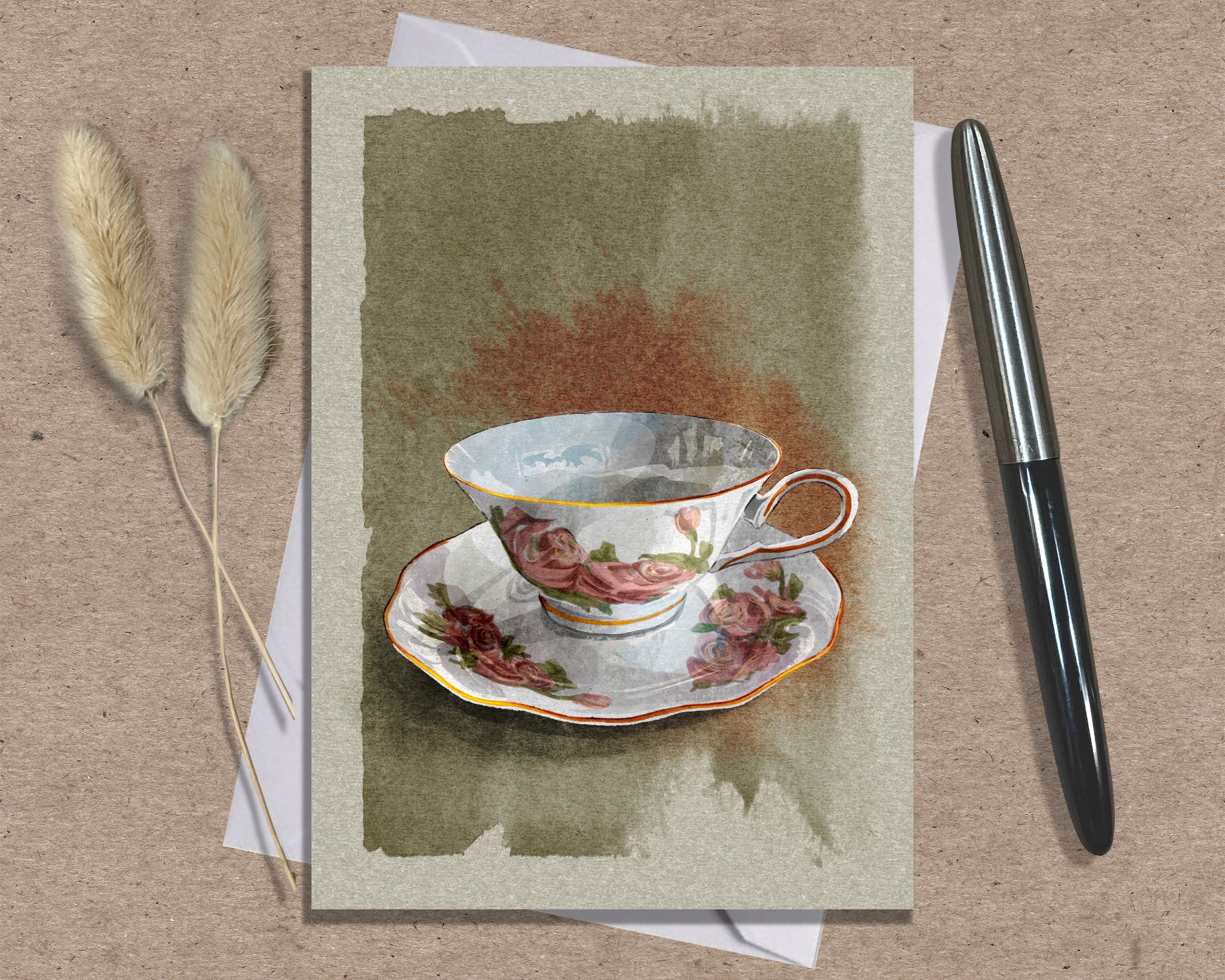 Greeting card with a teacup design on a textured surface with a pen and dried plants.
