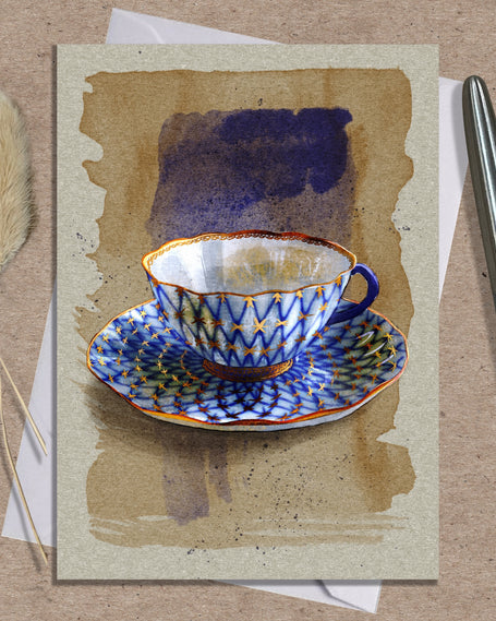 Greeting card with a blue and white teacup design on a textured surface with a pen and dried plants.