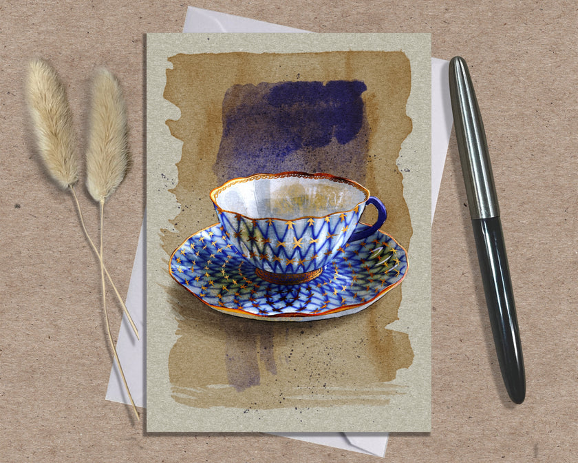 Greeting card with a blue and white teacup design on a textured surface with a pen and dried plants.