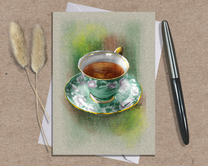 Greeting card with a painting of a teacup and saucer on a textured surface with a pen and dried plants.