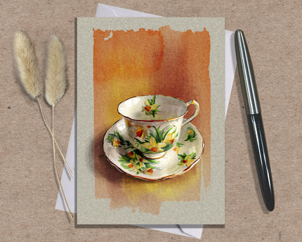 Greeting card with a teacup design on a textured surface with a pen and dried plants.