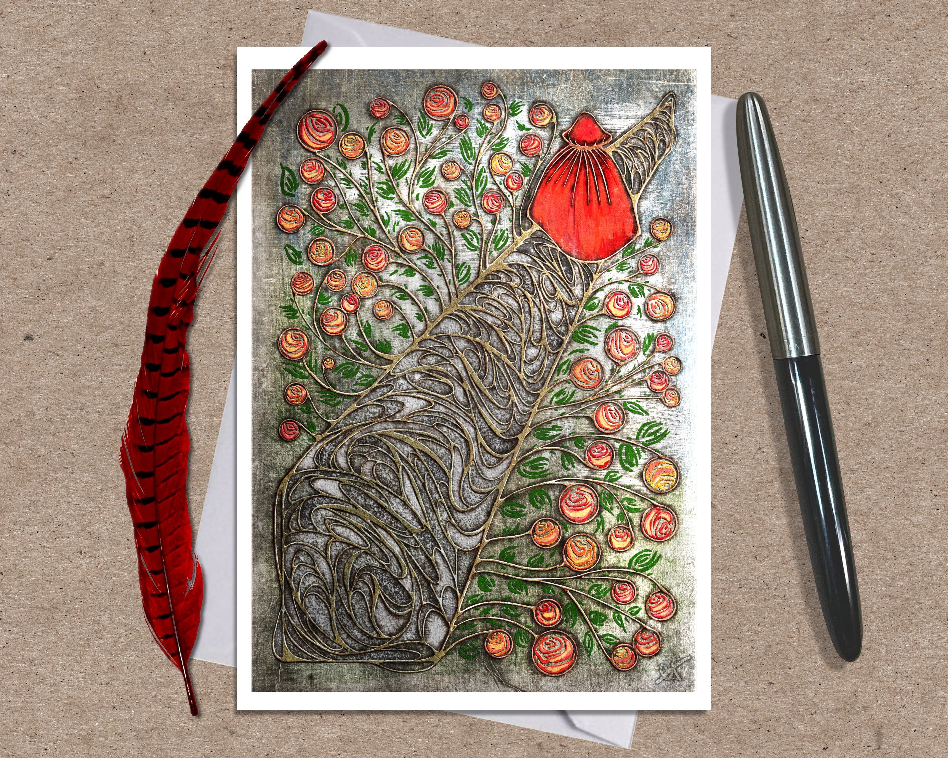 Greeting card with a stylized tree design featuring flowers and a red heart, placed on a textured surface with a pen and feather.