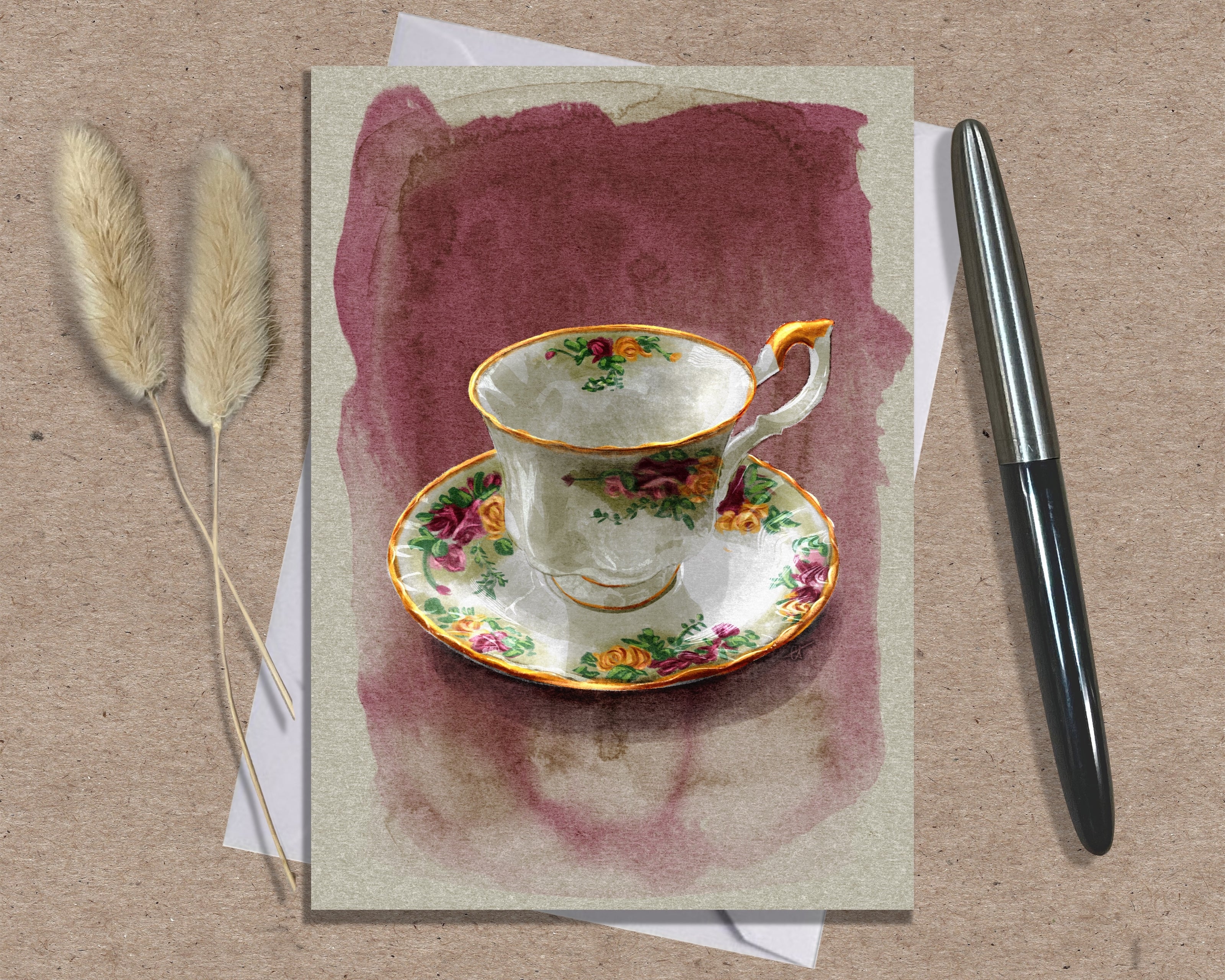 Greeting card with a floral teacup design on a textured surface with a pen and dried plants.