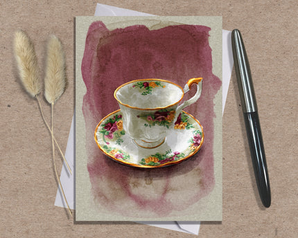 Greeting card with a floral teacup design on a textured surface with a pen and dried plants.