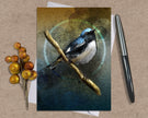 Greeting card with a bird illustration on a branch, surrounded by berries and a pen on a textured surface.