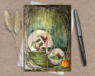 Decorative greeting card with nature-themed illustrations on a textured surface with a pen and dried plants.