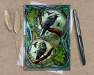 Decorative card with crow illustrations on a textured surface with a pen and dried plants.