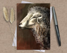 Greeting card with a sheep illustration on a textured surface with a pen and dried plants.