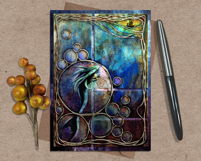 Decorative card with a mermaid design on a textured surface with a pen and decorative elements.