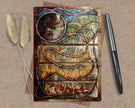 Decorative greeting card with artistic design on a textured surface with a pen and dried plants.