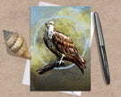 Greeting card with an osprey illustration on a textured surface with a shell and pen.