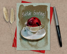 Greeting card with a red bell in a teacup, 'Yuletide Greetings!' text, and decorative elements on a textured surface.