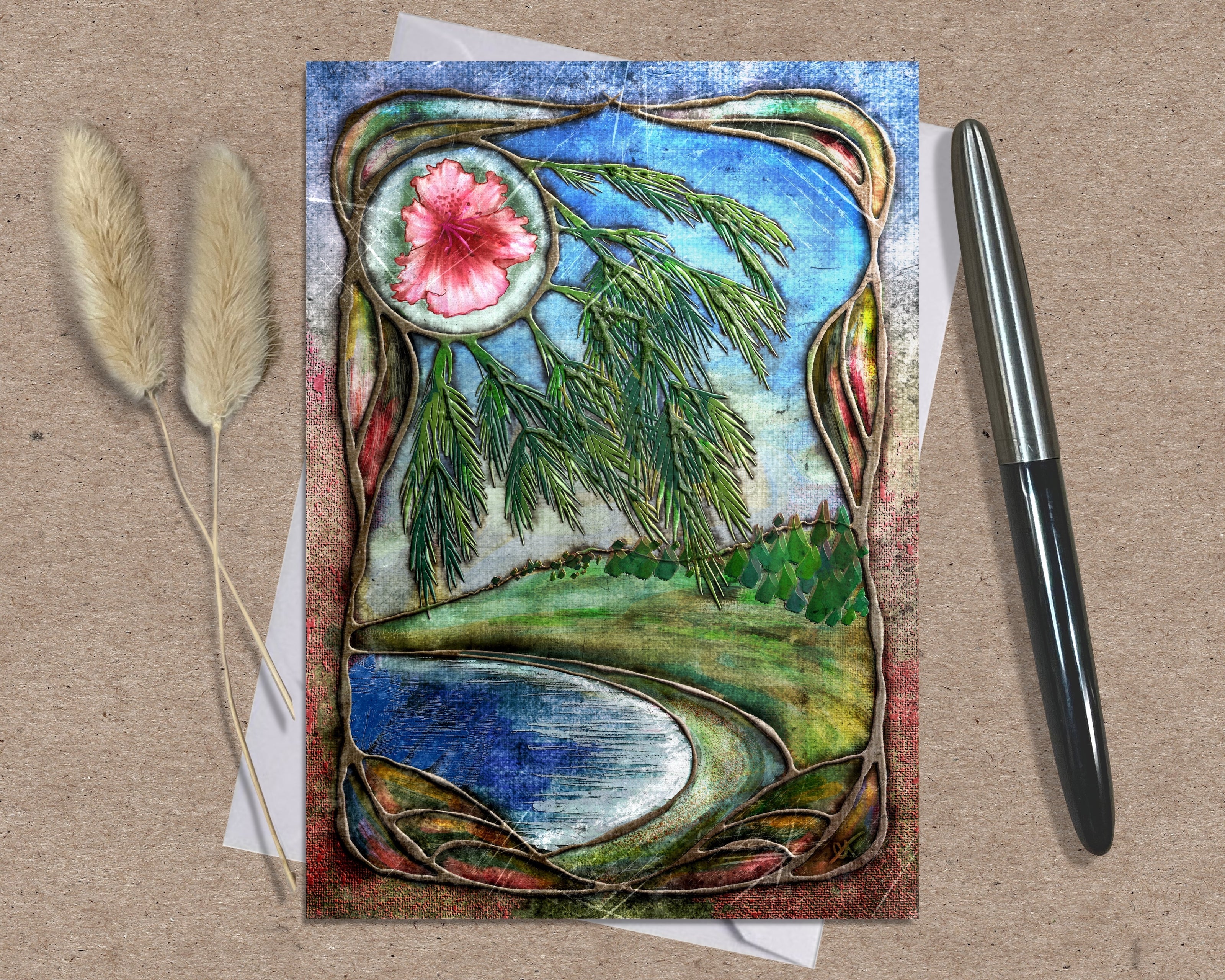 Decorative card with nature-themed design featuring a flower, trees, and water on a textured surface with a pen and dried plants.
