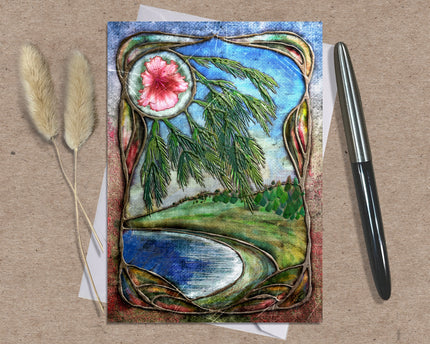 Decorative card with nature-themed design featuring a flower, trees, and water on a textured surface with a pen and dried plants.