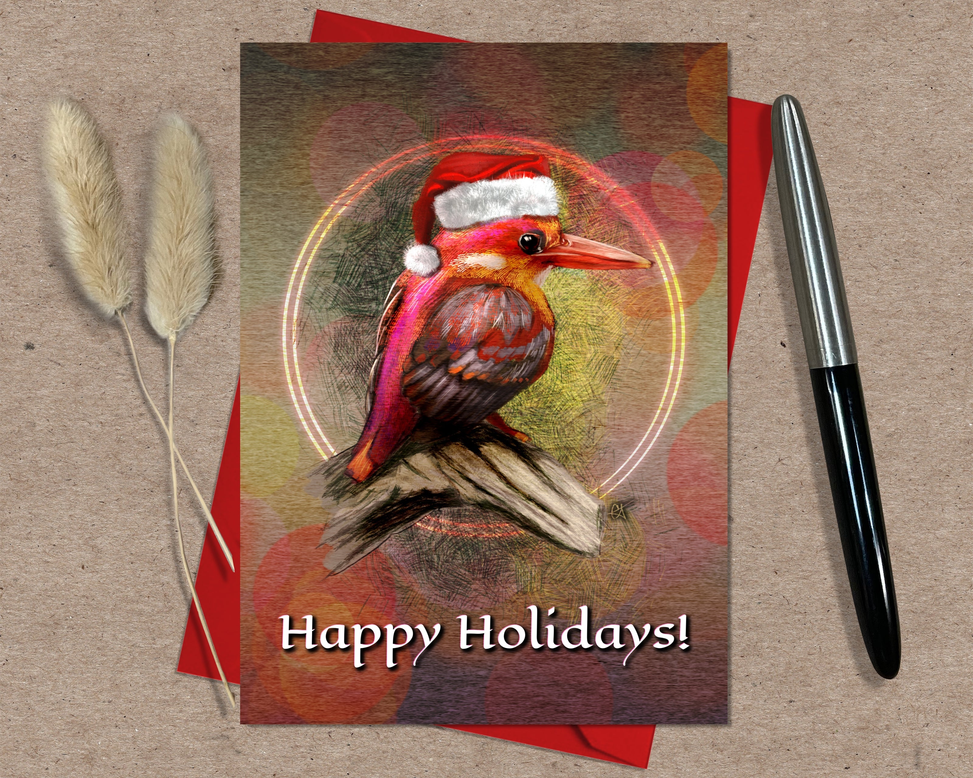 Greeting card with a bird wearing a Santa hat and 'Happy Holidays!' text, on a textured surface with a pen and dried plants.