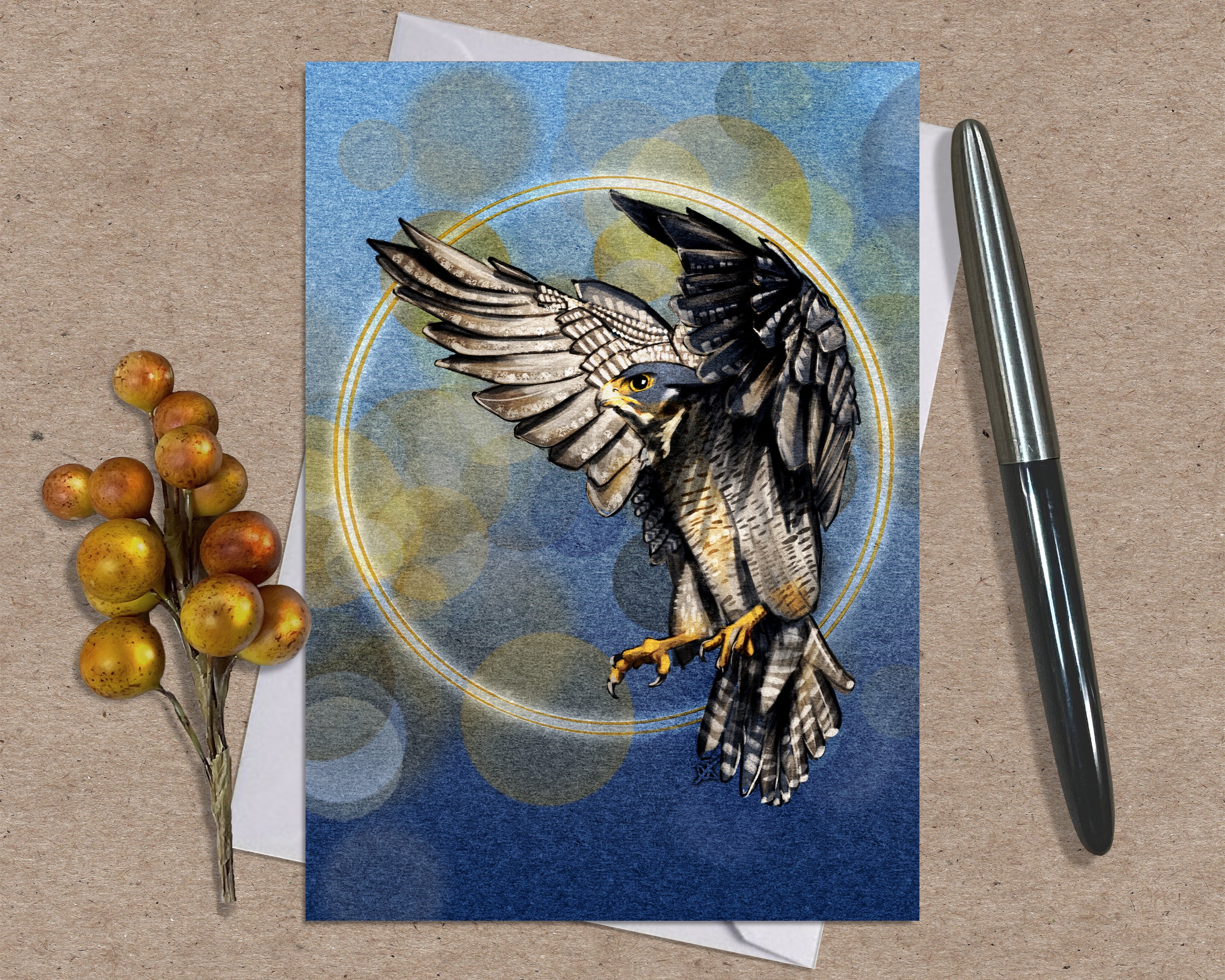 Greeting card with a falcon design on a textured surface with a pen and berries.