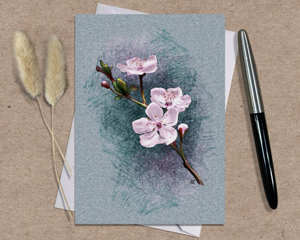 Greeting card with pink flowers on a textured blue background, accompanied by dried plants and a pen.