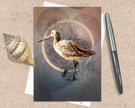 Greeting card with a bird illustration on a textured surface with a shell and pen.