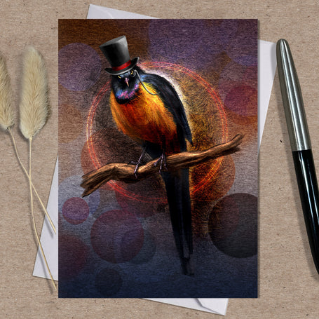 Greeting card with a stylized bird wearing a top hat on a textured surface with a pen and dried plants.