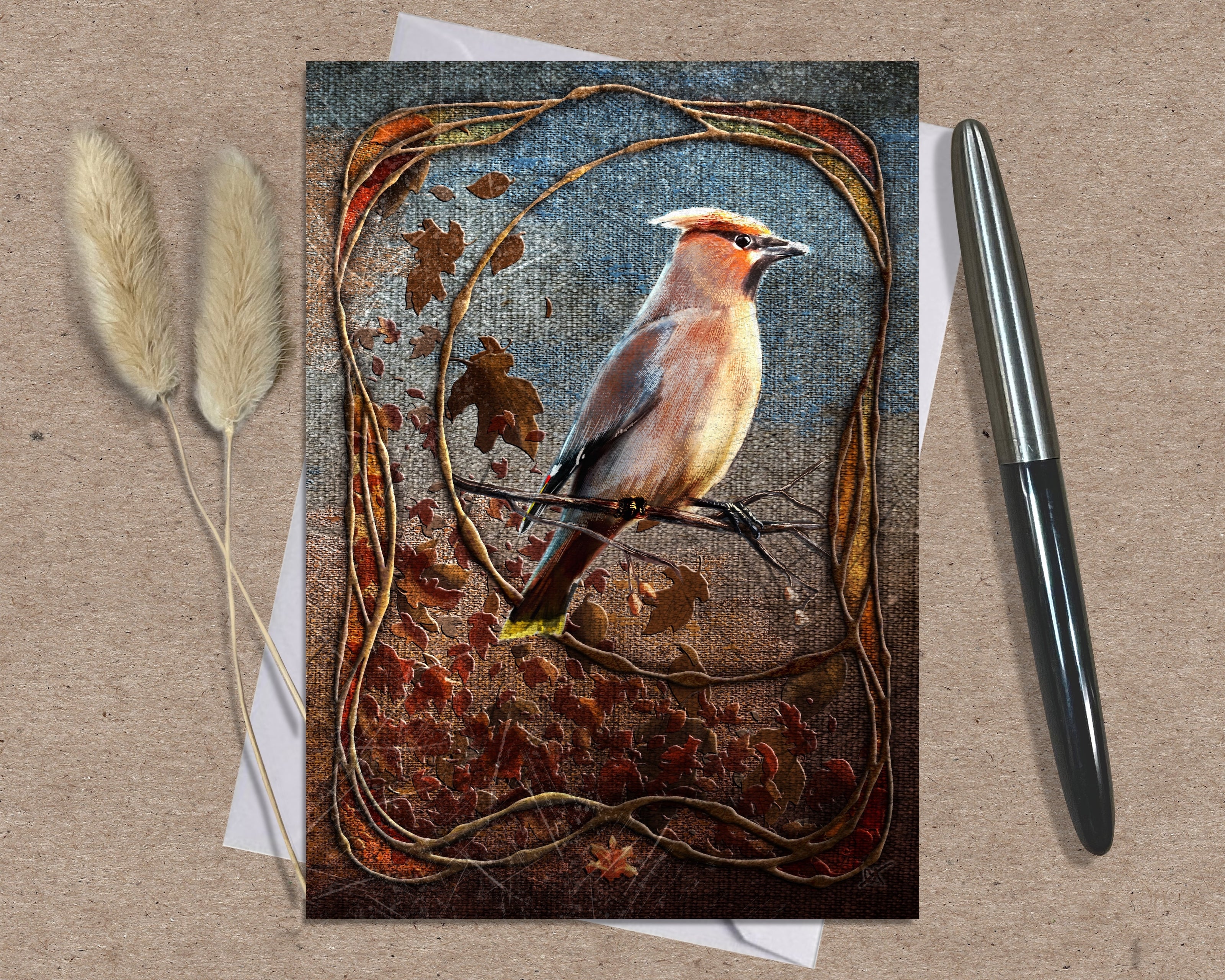 Greeting card with a bird design on a textured surface with a pen and dried plants.